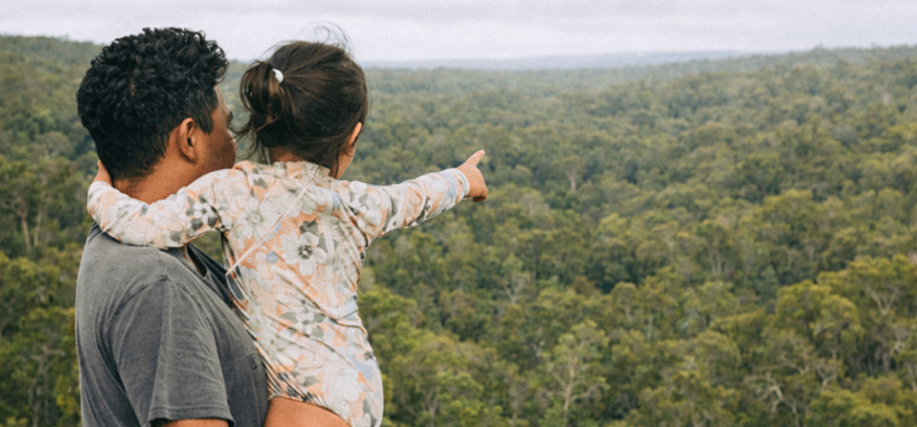 father and daughter pointing at a forest landscape